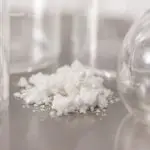 White CBD Isolate powder in a pile on a table with glassware in the background.